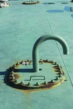 A green, curved pipe rises from a circular, bolted hatch on a teal surface. Stock Photos