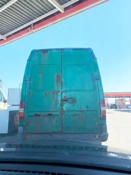 Green delivery van with rust spots parked at a gas station, visible fuel pumps Stock Photos