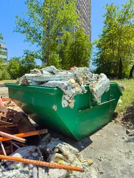 A green dumpster is filled with construction waste and debris. It is located  Stock Photos