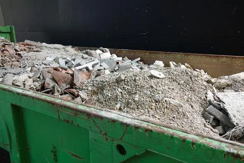 A green dumpster overflows with construction debris, including broken brick.. Stock Photos