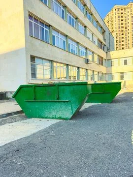 Green dumpster placed outside a building in an urban area during a sunny day Stock Photos