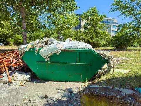 A green dumpster sits in a construction area filled with debris and old mater Stock Photos