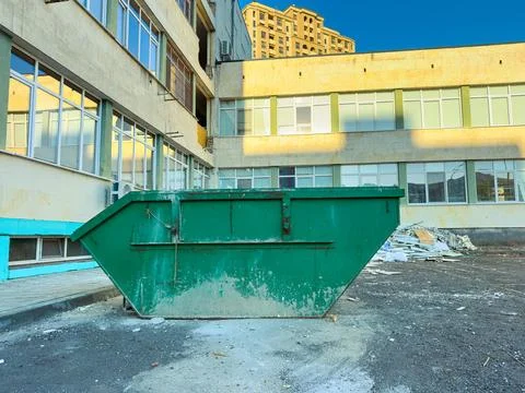 A green dumpster sits in a construction area beside a building that is being  Stock Photos