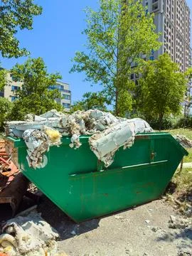 A green dumpster sits on a construction site. It is filled with torn material Stock Photos