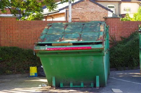 A green dumpster is sitting in front of a brick wall Stock Photos