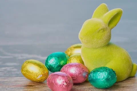Green easter bunny with chocolate eggs against wooden background Stock Photos