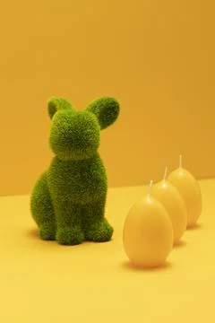 Green Easter Bunny with three yellow candles of eggs shape on matching Stock Photos