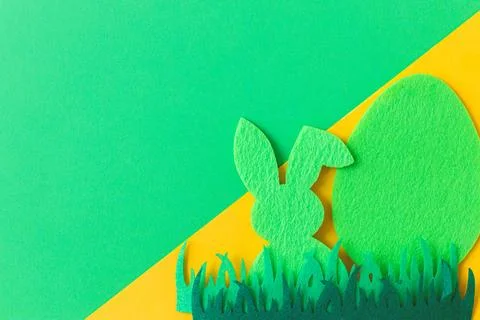 Green Easter egg and bunny in grass on green and yellow background, flat la.. Stock Photos