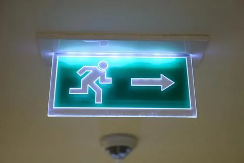 Green emergency exit sign with arrow glowing in the dark. Modern LED fire exit Stock Photos