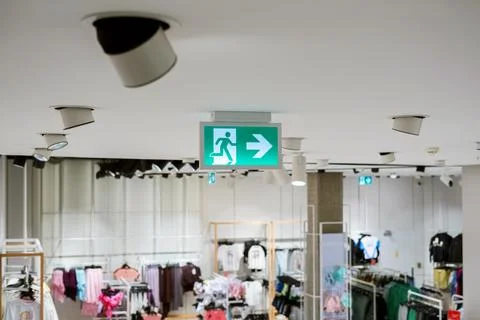 Green emergency exit sign with directional arrow hanging from ceiling in mo.. Stock Photos
