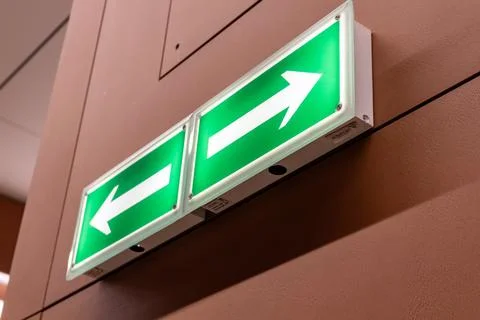 Green emergency exit sign with left and right arrows on brown wall Stock Photos