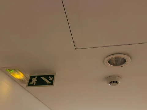 Green emergency fire exit sign is placed on the ceiling along the corridor... Stock Photos