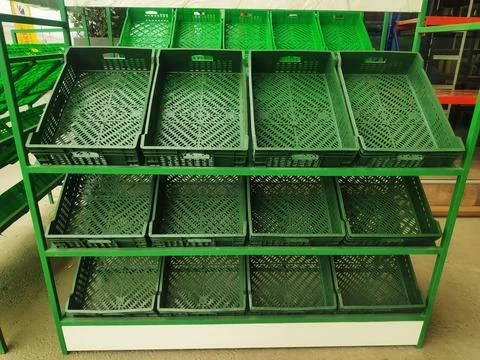 Green empty plastic boxes are on the shelves for various products and fruit.. Stock Photos