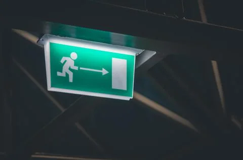 Green exit sign hanging from the ceiling. Fire exit sign. Selective focus, copy Stock Photos