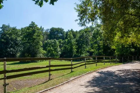 Green field secured with a split-rail fence by the road Stock Photos