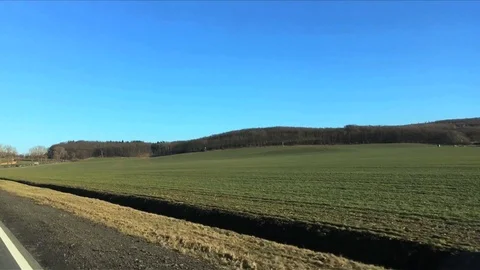 Green fields against hills with trees in early spring. View from moving car wind Stock Footage 104576648
