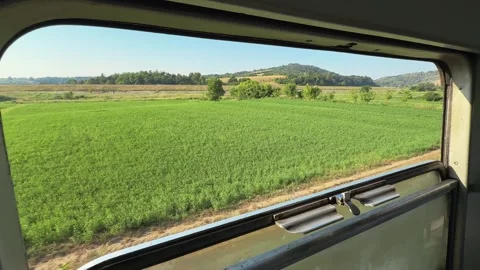 Green fields and hills pass outside an open train window in Montenegro. Railway Stock Footage 344900656