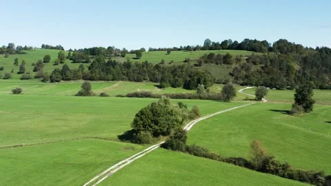 Green fields stretch into distance, bordered by trees and hills under blue sky. Stock Footage 287114463
