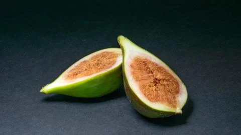 Green figs, one fruit cut into two halves on a light dark background Stock Photos