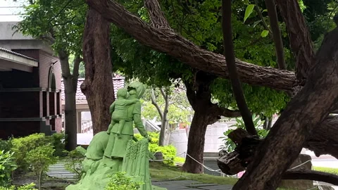 Green Figure Sculpture Under Twisting Branches In A Shaded Garden Stock Footage 344240600