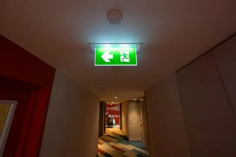 A green fire exit sign hangs from the ceiling with a running man and right .. Stock Photos