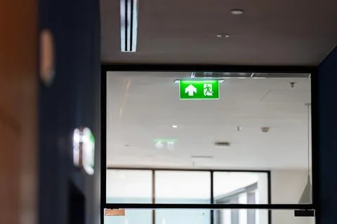A green fire exit sign hangs from the ceiling with a running man and right .. Stock Photos