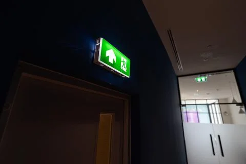 A green fire exit sign hangs from the ceiling with a running man and right .. 스톡 사진