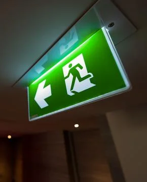 A green fire exit sign hangs from the ceiling with a running man and right .. Stockfoto's