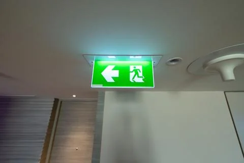 A green fire exit sign hangs from the ceiling with a running man and right .. 库存照片