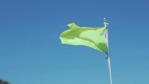 Green flag blowing in clear blue sky Stock Footage 77525156