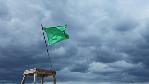 Green flag waves on a post while dark clouds gather in the sky during the early Stock Footage 337877444