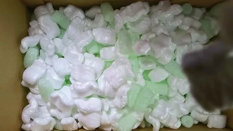 Green foam rubber and white styrofoam filler falls into a cardboard box Stock Footage