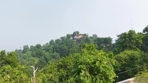 Green forested hill with a small temple under clear daylight sky Vidéo 347763704