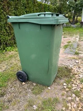 Green Garbage Bin with Crack on Grass Near Metal Drainage Grate Stock Photos