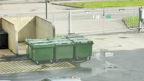 Green garbage bins sit quietly outside near a metal gate Video stock 344984119