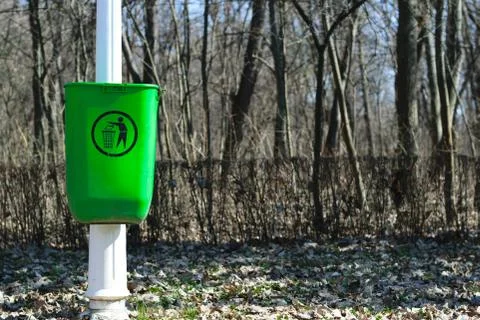 Green garbage can on white pole in park - spring time - midday Stock Photos
