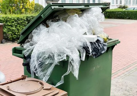 Green garbage container bin overflowing with plastic packaging waste Foto stock