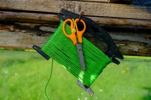 Green garden string on a spool and scissors with orange handles hung on a nai Stock Photos