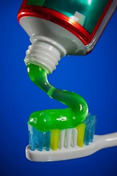 Green gel toothpaste being squeezed from tube onto colorful toothbrush bris.. Stock Photos