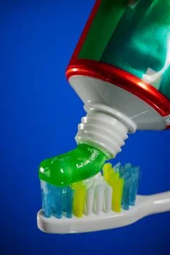 Green gel toothpaste being squeezed from tube onto colorful toothbrush bris.. Stock Photos
