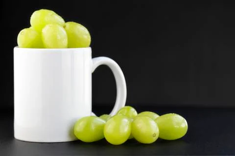 Green grapes portion inside a white mug on black background with copy space.. Fotos Stock