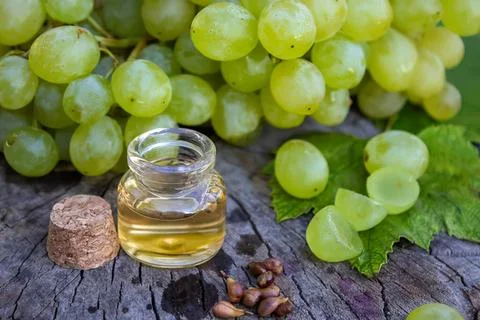 Green grapes with small jar of grape seed oil on wooden surface Stock Photos