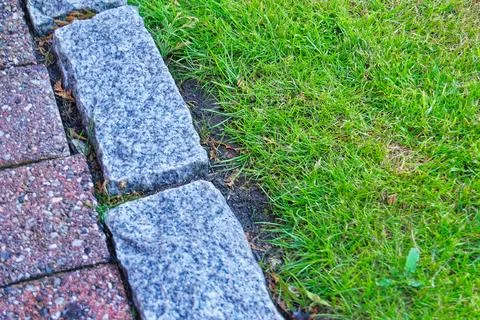 Green grass bordered by stone and brick paving in an outdoor garden setting Stock Photos
