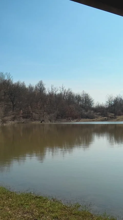 Green grass borders the calm lake surface. Balkan, Eastern Europe, POV Video stock 333634561