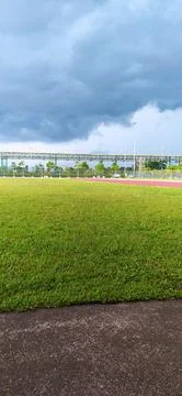 Green grass field under dramatic dark storm clouds with blue sky Stockfoto's