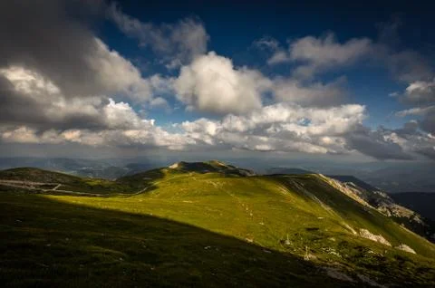 Green grassy plateau with big patch of shade and dramatic, cloudy, dark blue sky Stock Photos