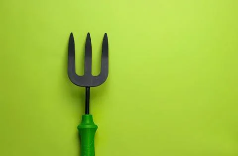 Green-handled garden fork on bright green background Stock Photos