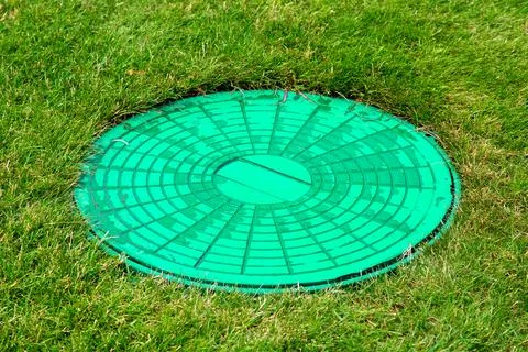 Green hatch of sewer system in clearing with green grass, close up manhole. Stock Photos