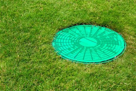 Green hatch of a sewer system in a clearing with green grass. Stock Photos