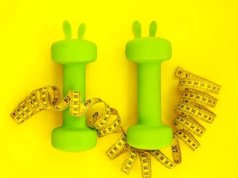 Green heavy dumbbells in shape of easter bunny and yellow tape measure on yellow Foto stock